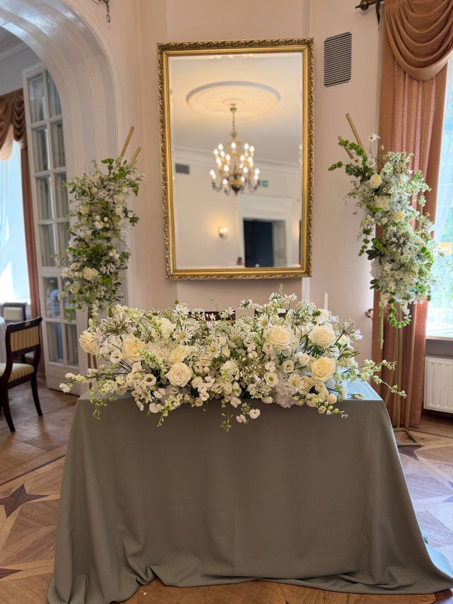 Dwie wysokie kompozycje kwiatowe i biała aranżacja florystyczna w eleganckim wnętrzu